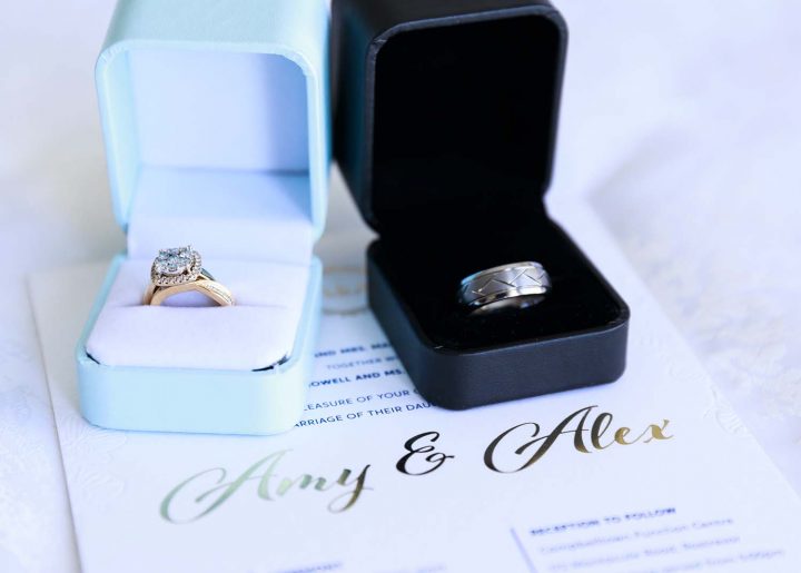 Wedding rings in ring boxes sitting on top of a wedding invitation